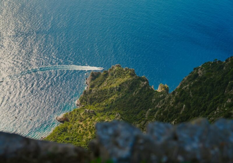 A private boat cruising past green cliffs on the Italian coast